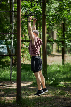 Vertical shot of young adult Caucasian man training on outdoor monkey bars, building upper body strength in park. Fitness motivation concept for workout, wellness, active lifestyle marketing