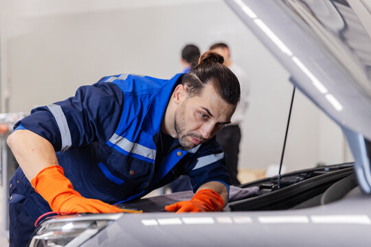 Focused EV Technician Inspecting Electric Vehicle During Professional Maintenance in Modern Service Workshop
