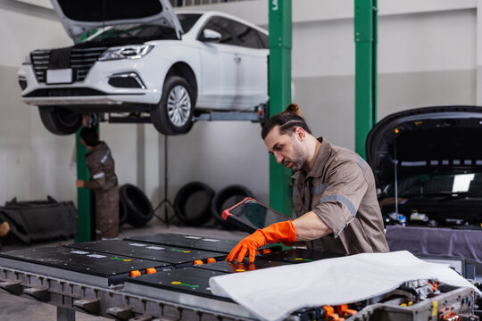 Professional EV technician inspecting a high-voltage battery pack using a digital diagnostic tablet in a modern electric vehicle service workshop.