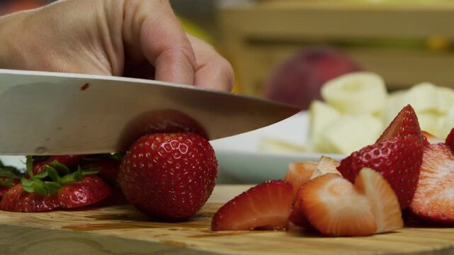 Knife dicing up delicious, juicy strawberry on chopping board - closeup, slow motion shot