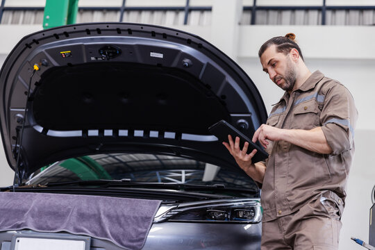EV Technician Using Digital Tablet for Electric Vehicle Diagnostics in Modern Service Workshop
