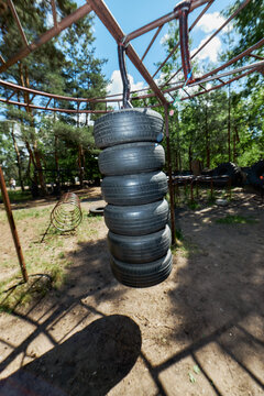 Vertical shot of stacked tires hanging from outdoor obstacle course frame, creating fitness challenge in forest setting. Suitable for boot camp, teamwork, endurance training promotion