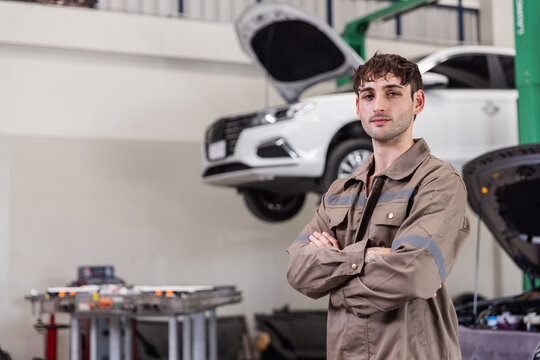 Confident EV Service Engineer Standing in Modern Electric Vehicle Repair Workshop with High Voltage Battery Expertise