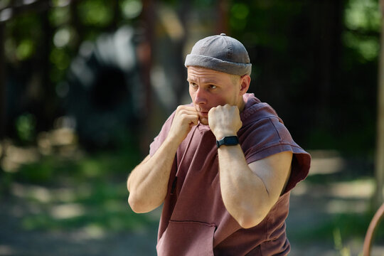Young adult Caucasian man raising fists in boxing guard, training outdoors and focusing on fitness discipline. Useful for sports marketing, workout apps, healthy lifestyle campaigns