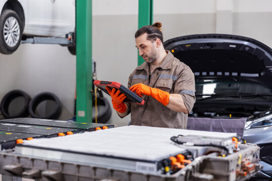 EV Technician Performing High Voltage Battery Diagnostics with Professional Scan Tablet in Electric Vehicle Repair Workshop