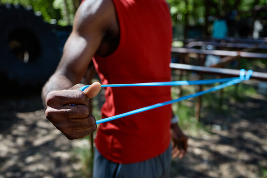 Close up of Black young adult man stretching resistance band during outdoor workout, building strength and fitness discipline. Ideal for sports training, wellness, active lifestyle marketing
