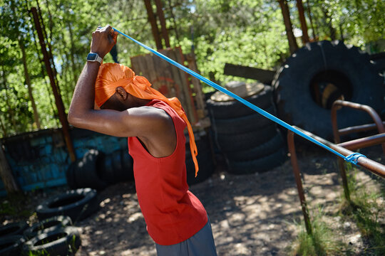 Black young adult man exercising with resistance band outdoors, strengthening shoulders and arms during functional workout. Fitness, endurance, personal training, healthy lifestyle marketing