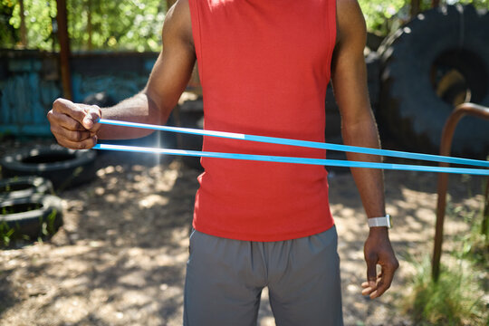 Black young adult man stretching resistance band during outdoor workout, building strength and fitness discipline. Useful for sports training, wellness, exercise promotion