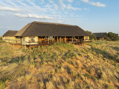 Kgalagadi South, Botswana - 06 February 2026: Aerial view of Tashebube, Rooiputs Lodge with its traditional thatched roof and wooden deck set amidst the arid sand dunes and dry grasses.