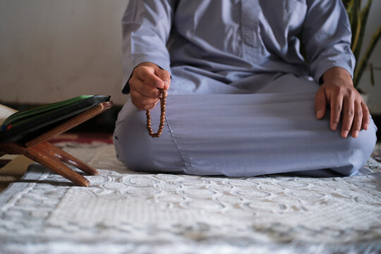 Close-up of hands reciting dhikr using prayer beads with a blurred background. Hands reciting dhikr. A man reciting dhikr while holding a prayer bead. Front view photo
