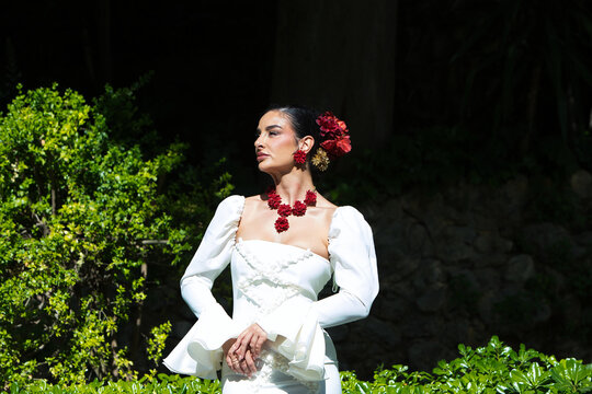 A beautiful woman dancing flamenco in a park in Seville, Spain. She is wearing a traditional white dress with ruffles and has red flowers in her hair. Flamenco, a UNESCO Intangible Cultural Heritage.