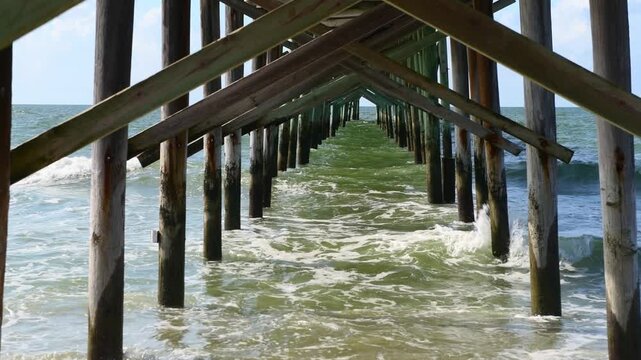 Ocean waves breaking under a wooden pier