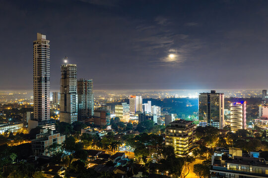 Asuncion, Paraguay - 12 July 2025: Aerial view of Las Lomas district skyline at night with illuminated skyscrapers, residential buildings, and a bright moon in the dark sky.