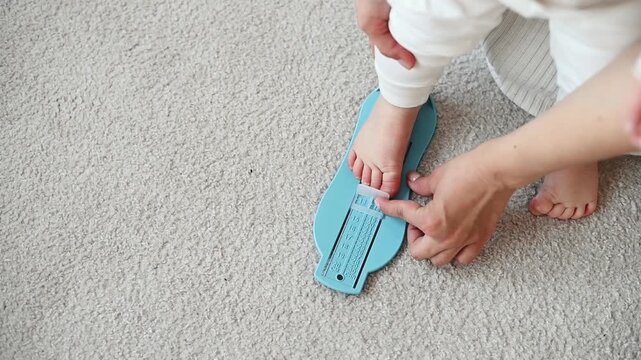 Close-up of a young mother measuring her one year old daughter's foot using a children's foot measuring tool before choosing the correct shoe size.