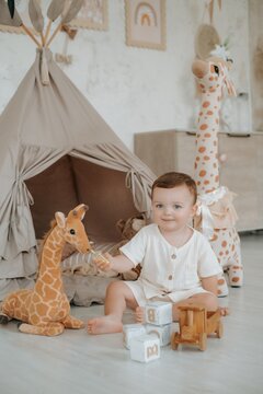 a child plays in a children's room with a teepee, wooden blocks, and a car on the floor among stuffed giraffes, a small boy playing at home