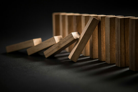 Falling wooden domino blocks on dark surface, close-up of chain reaction and collapse concept for risk, failure or cause and effect business ideas
