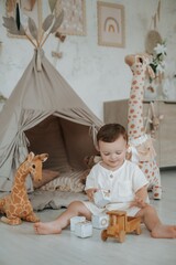 a child plays in a children's room with a teepee, wooden blocks, and a car on the floor among stuffed giraffes, a small boy playing at home © Any Grant