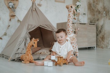 a child plays in a children's room with a teepee, wooden blocks, and a car on the floor among stuffed giraffes, a small boy playing at home © Any Grant