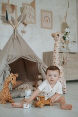 a child plays in a children's room with a teepee, wooden blocks, and a car on the floor among stuffed giraffes, a small boy playing at home © Any Grant