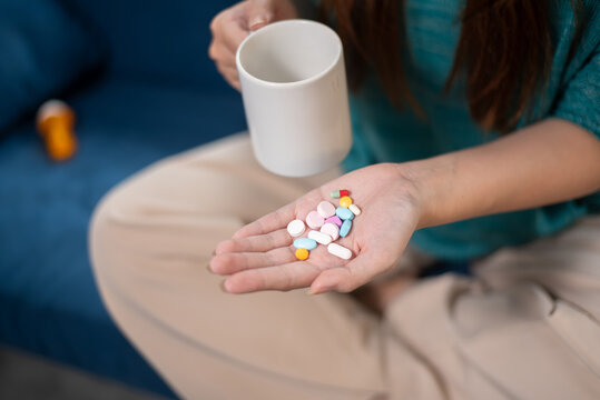 Woman Holding Multiple Colorful Pills and Tablets in Palm with White Mug, Daily Medication Concept