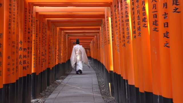 A Shinto priest walking through the iconic torii gates at Fushimi Inari Shrine in Kyoto, Japan, slow motion shot.