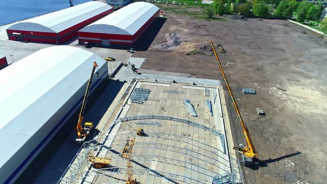 Aerial view of construction site with mobile cranes assembling a metal frame structure near large warehouses in Riga, Latvia.