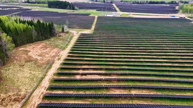 Aerial view of a large solar farm with rows of photovoltaic panels installed in a rural landscape near a forest in Latvia.