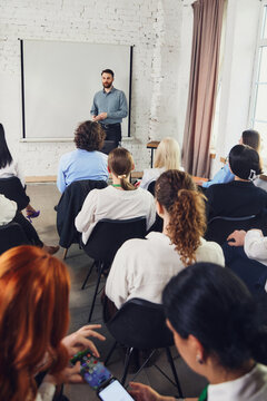 Male speaker presenting to business audience in modern training room. Concept of corporate seminar, employee education, leadership workshop, coaching, and professional event content.