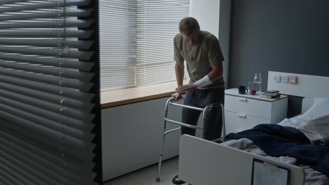 Caucasian man with bandaged arm standing with walker in hospital room, preparing for rehabilitation. Footage for medical equipment and physical therapy marketing