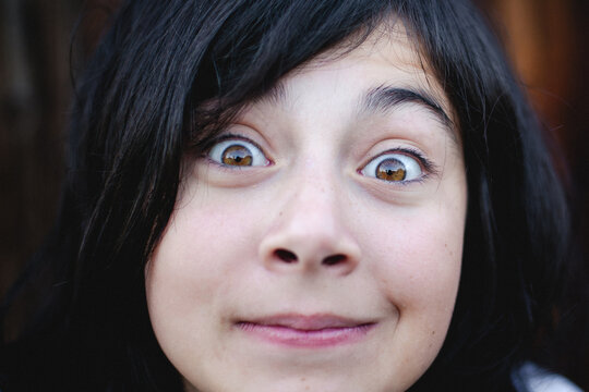Close up portrait of a funny young girl making a silly face with wide open eyes and looking directly at the camera