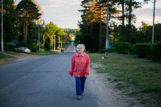 Senior woman walking alone along a quiet village road during golden hour in a peaceful rural landscape