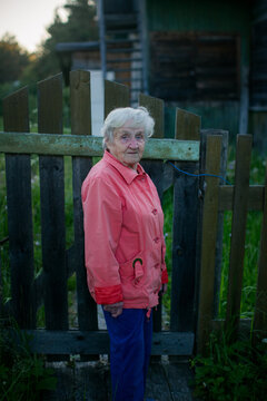 Senior woman standing by a rustic wooden gate in a quiet countryside village at dusk