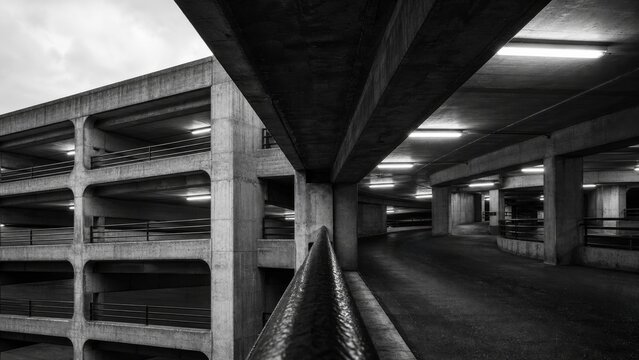 A monochrome image of a concrete parking garage, showcasing its architectural lines and structure with contrasting shadows and light.