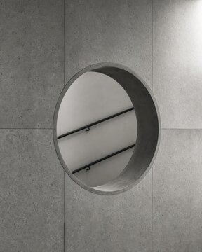 A circular opening in a textured gray wall reflects a staircase, creating a modern and minimalist aesthetic.