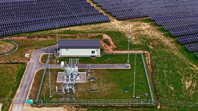 Aerial view of a solar farm and electrical substation with rows of photovoltaic panels and power equipment in Latvia.