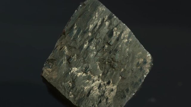 A cubic crystals of pyrite, with some surfaces showing characteristic striations, isolated on a black background
