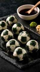 Fototapeta premium Six soccer ball shaped onigiri arranged on a dark slate platter with soy sauce, wasabi, and pickled ginger in a studio shot