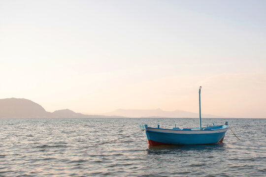 Small greek boat in the sea at sunset with mountains on the background