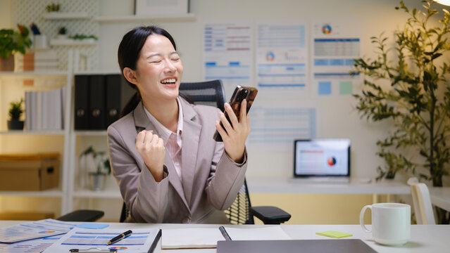 Excited businesswoman cheering after receiving a positive message or successful business update on her mobile phone.