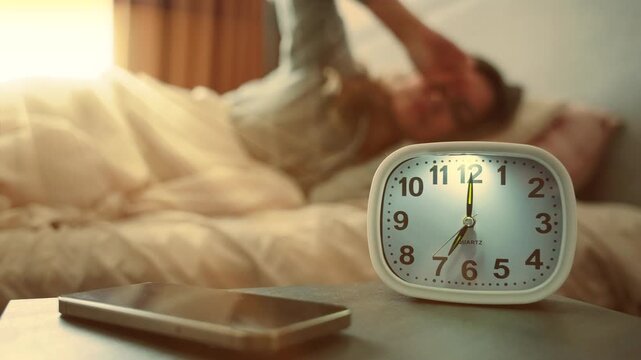 woman waking up on sunny morning close-up hand turning off alarm clock, getting out of bed. Healthy sleep cheerful active girl. beautiful stylish modern bedroom. closeup clock shows 7:00 AM sun light