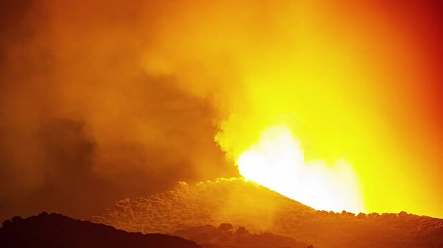 View of a powerful volcanic eruption at night with glowing lava and thick plumes of smoke rising above the dark silhouette of the hills in Spain.