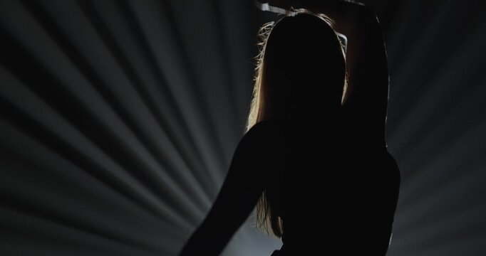 Silhouette of a female dancer performing on a dark stage, back lit by dramatic volumetric light rays with copy space. Concepts related to dance, self discovery, album covers, singles, or podcasts