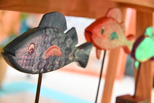 handcrafted wooden fish sculptures on metal stands close up, colorful painted fish figurines on display, rustic coastal decor craft, traditional brazilian wooden handicraft with copy space