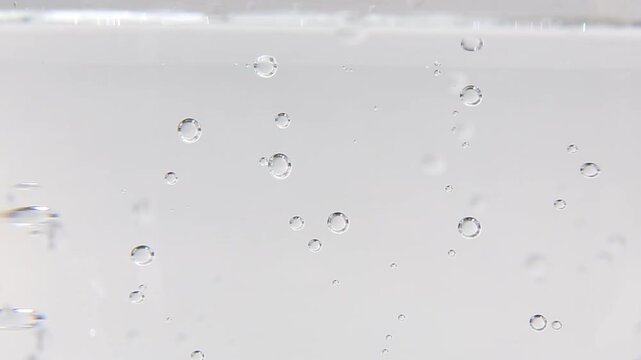 Clear water fills the frame in close-up as small bubbles float and drift slowly upward and sideways across the glass surface, creating a calm and satisfying ASMR scene throughout.