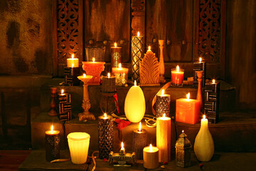 View of an assortment of decorative candles of various shapes, sizes, and textures glowing warmly on stone steps in a dimly lit room in Lahore, Punjab, Pakistan. © Paul