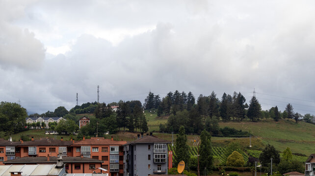Pueblo frente a colina arbolada bajo cielo nublado