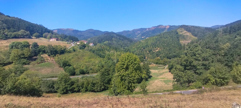 Paisaje monta&ntilde;oso verde con &aacute;rboles y peque&ntilde;a casa rural bajo cielo azul