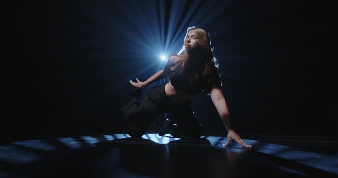 Attractive female dancer posing on floor under bright blue spotlight. Concept of expressive artistic layout for music album cover, theater poster and modern dancing class promotion.