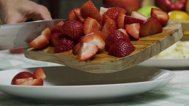 Closeup shot of knife scrapping diced strawberries onto plate in slow motion