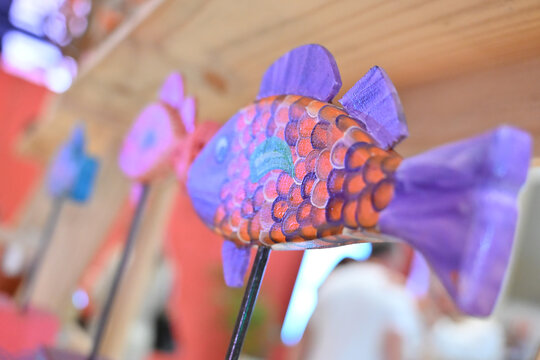 handcrafted wooden fish sculptures on metal stands close up, colorful painted fish figurines on display, rustic coastal decor craft, traditional brazilian wooden handicraft with copy space